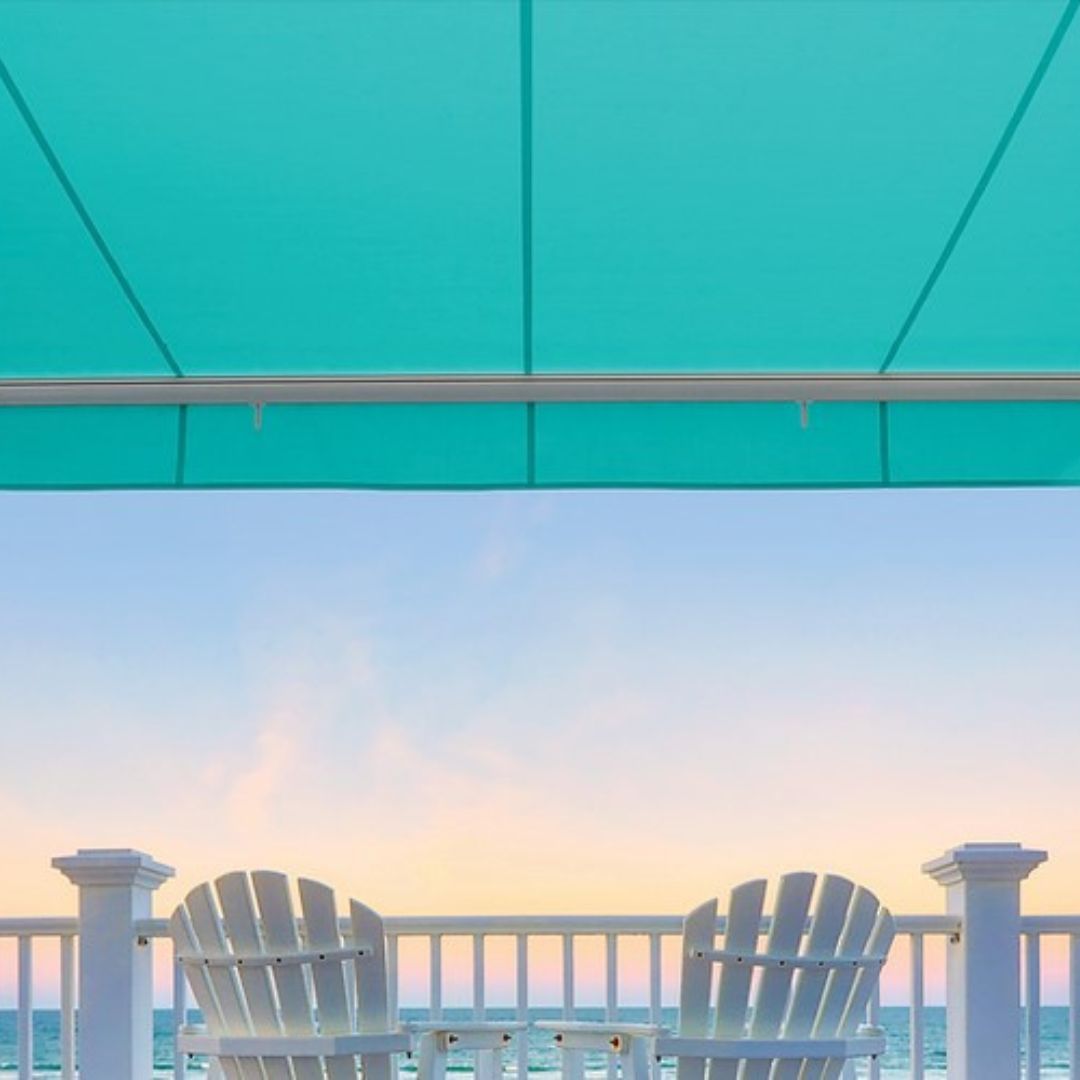 Interior shot of a patio with a teal retractable awning facing a body of water at sunset. The right color retractable awning for a home depends on how much light and heat you want to reflect in areas like this.