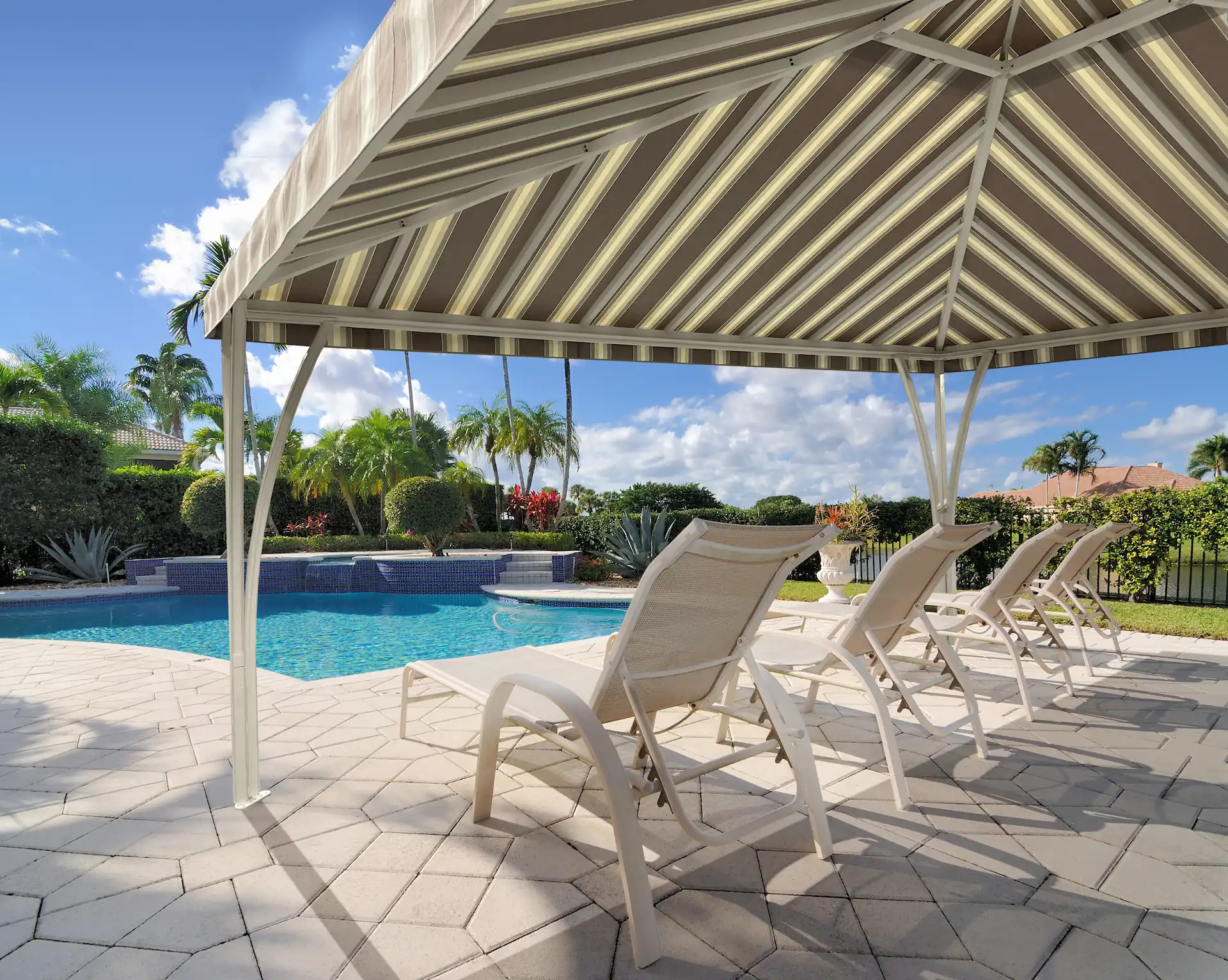A cabana with a grey and white striped covering sits in the sun next to a pool. Enjoying the scenery and resting your body are just two of the activities to do in a cabana like this.