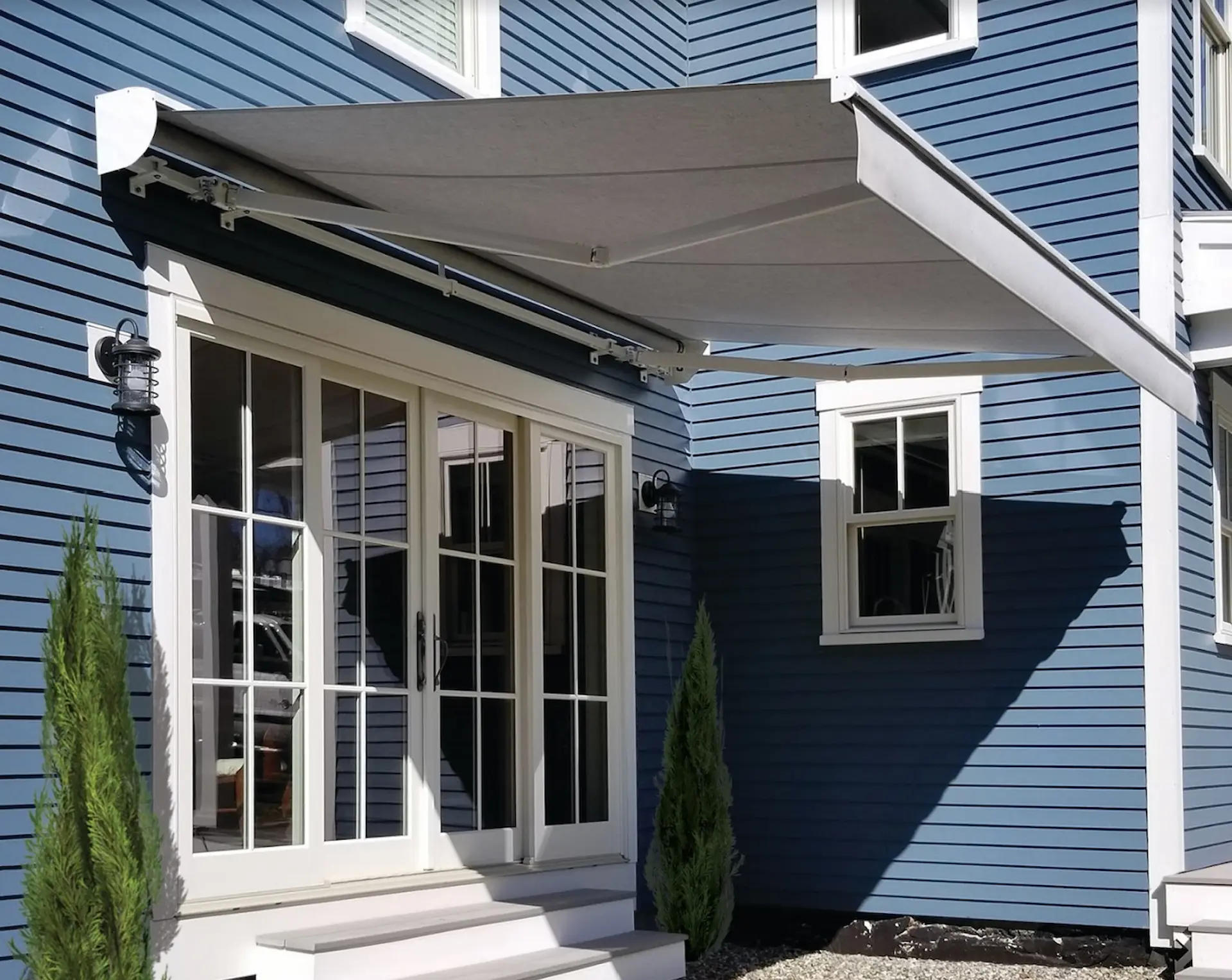 A grey retractable awning is extended from the back door of a blue house,