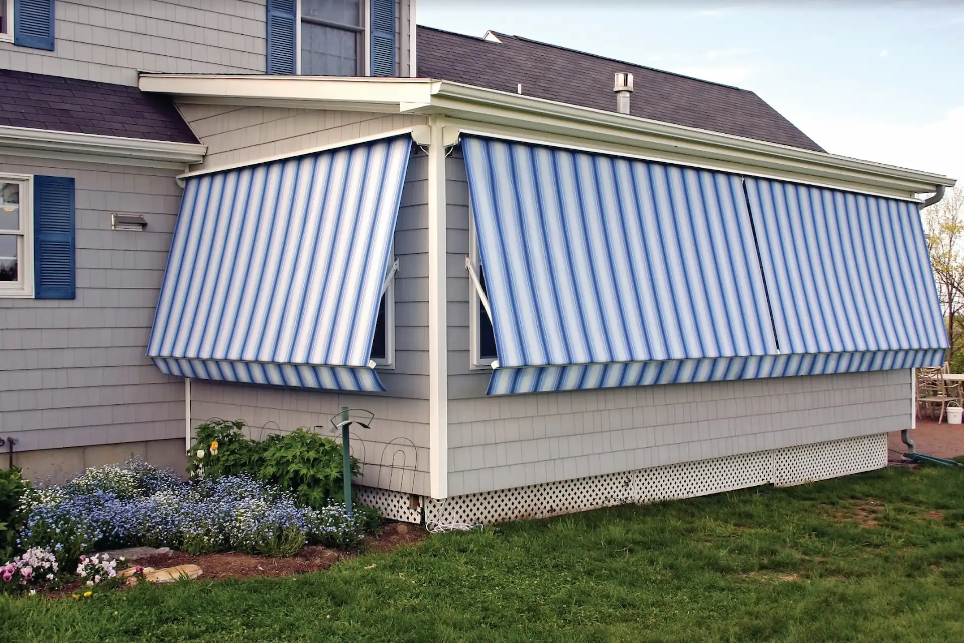 Exterior shot of a set of blue and white-striped window awnings are pulled down over the windows of a sunroom. When it comes to how to clean your awning, you should always wash and dry it in its fully extended position.
