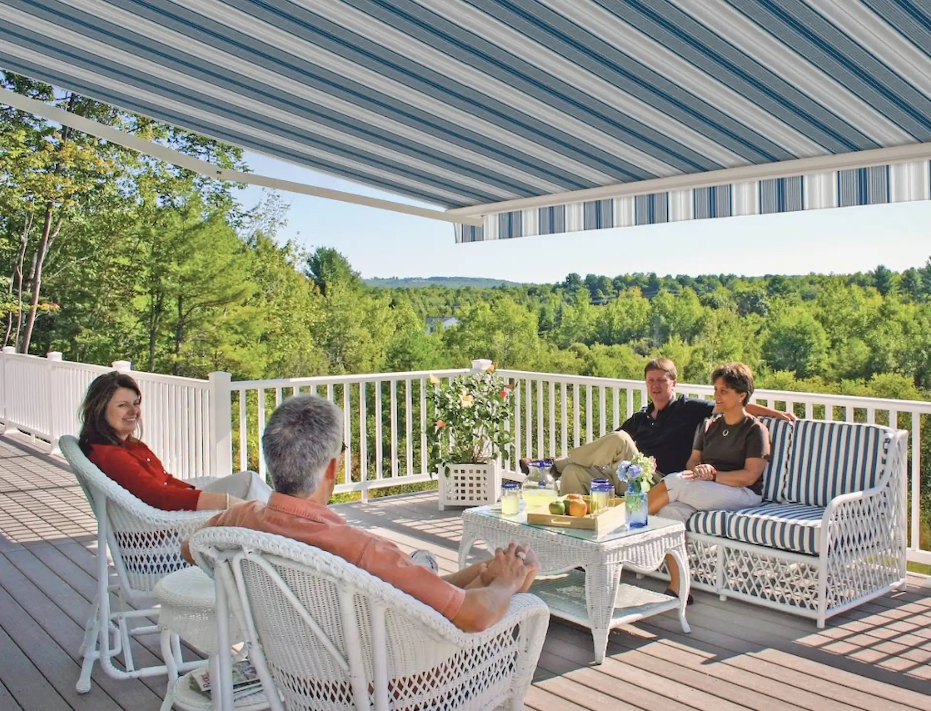 Medium shot of four guests enjoying a drink on a patio covered by a striped retractable awning.