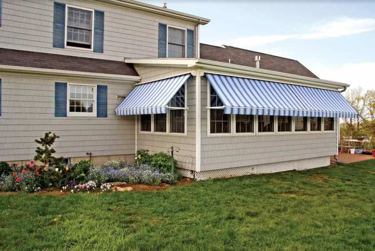 Exterior shot of a sun room with a blue-and-white striped modern window awning on each side.