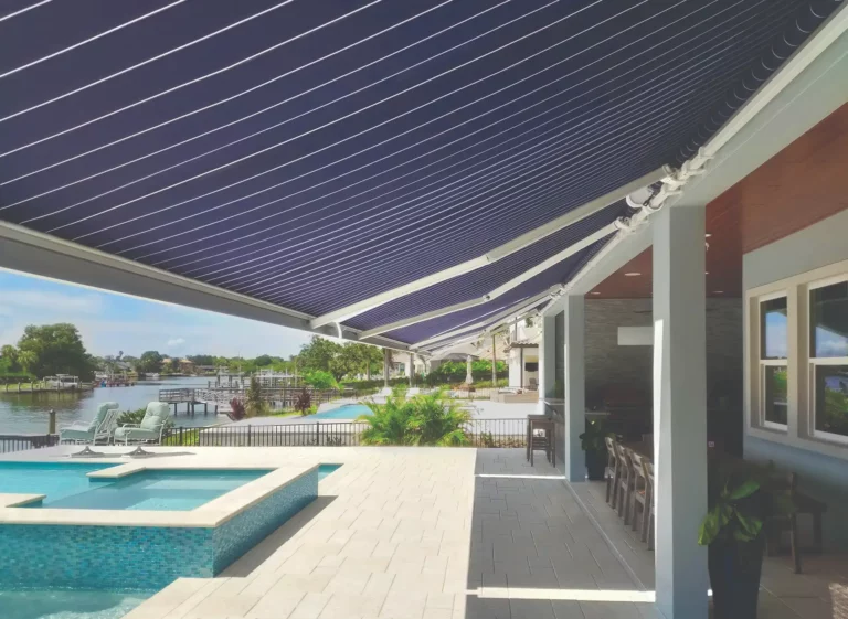 A retractable awning with dark blue background and thin white stripes is extended from the side of a home.
