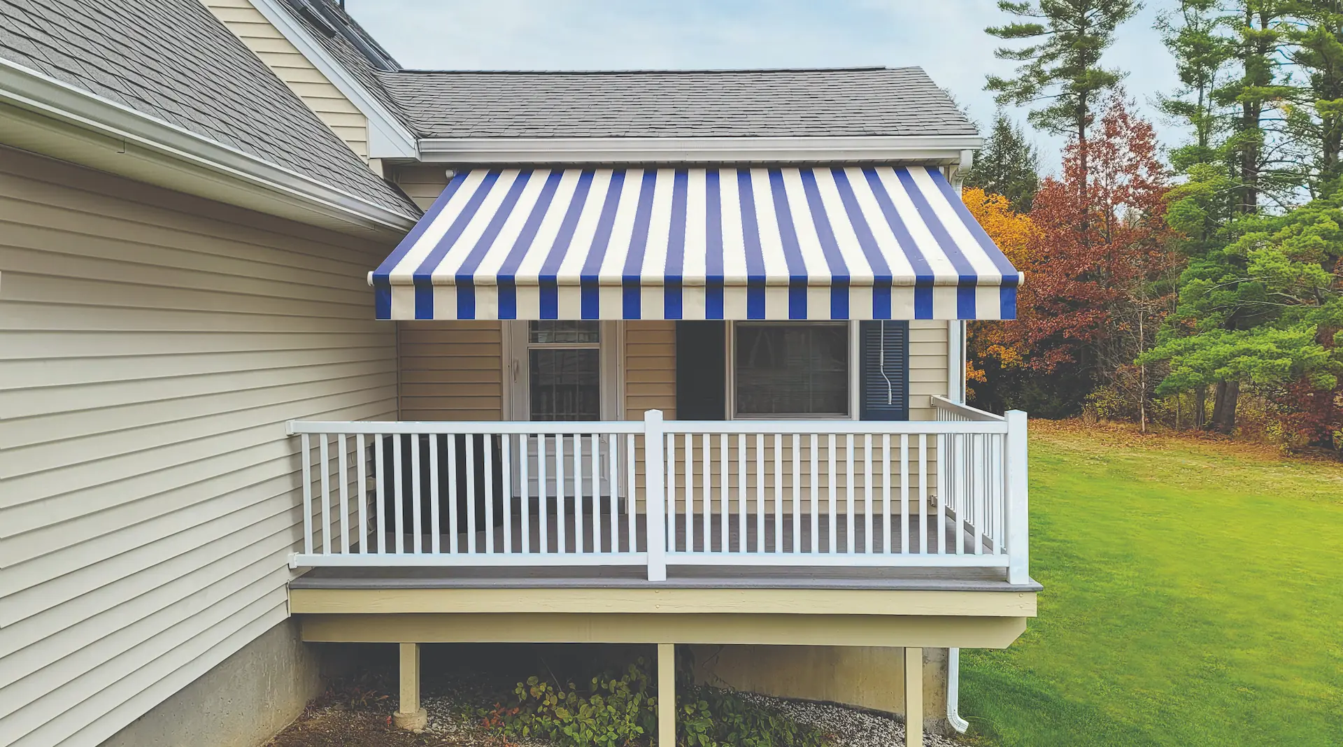 A retractable awning with blue and white stripes is extended to enhance the privacy of the rear window of a house.