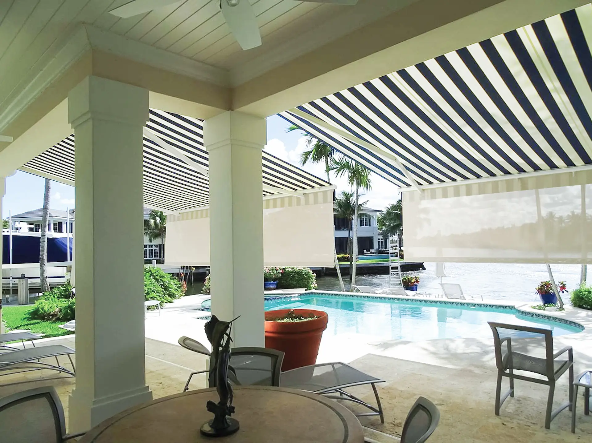 Interior shot of 2 retractable awnings with blue and white stripes extended on an elegant pool deck.
